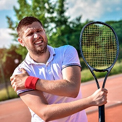 Man holding tennis racket, suffering from shoulder pain