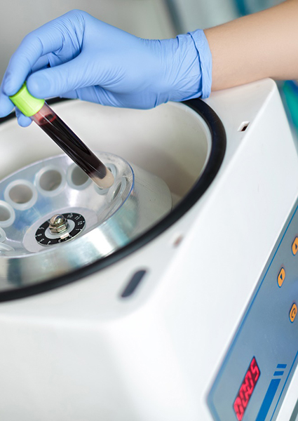 Gloved hands placing vial of blood in centrifuge